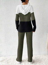 Woman wearing a moss, black and white color block half zip hooded top with matching ribbed-look pants.