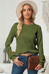 Woman wearing a moss textured round neck long sleeve blouse with dark-wash jeans, brown clutch and cream hat.