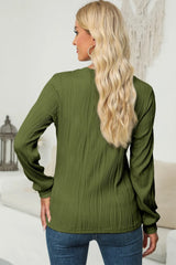 Woman wearing a moss textured round neck long sleeve blouse with dark-wash jeans.