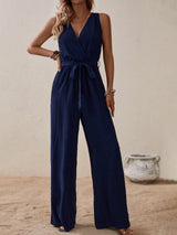 Woman wearing the Honey Tied Surplice Sleeveless Wide Leg Jumpsuit in navy with a tie waist and wide-leg silhouette, elegant women's one-piece outfit from Chic Mystik Boutique.