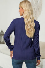 Woman wearing a navy textured round neck long sleeve blouse with dark-wash jeans.