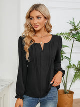 Woman wearing a black notched neck long sleeve blouse with flounce cuffs styled with light-wash jeans and a black handbag.