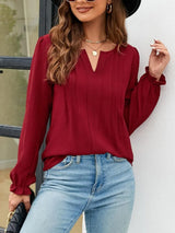 Woman wearing a burgundy notched neck long sleeve blouse with flounce cuffs styled with light-wash jeans and a black handbag.