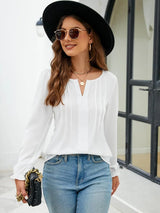 Woman wearing a white notched neck long sleeve blouse with flounce cuffs styled with light-wash jeans and a black handbag.