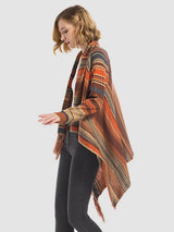 Woman wearing the Angel Wings tassel striped open-front cardigan in ochre, featuring earthy multicolor stripes, a draped asymmetrical front, and long fringe trim.