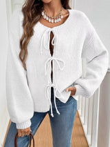 Woman wearing an off-white tie-front long sleeve knit cardigan with three bow ties paired with blue jeans.