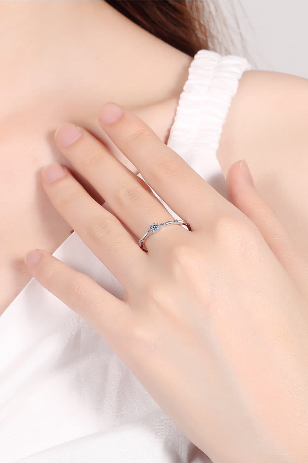 Rhodium-plated 925 sterling silver minimalist ring featuring a 0.1 carat round moissanite center stone with delicate sparkling accents on a teal background.