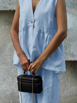 Person wearing a light blue sleeveless top holding a black handbag against a concrete wall.