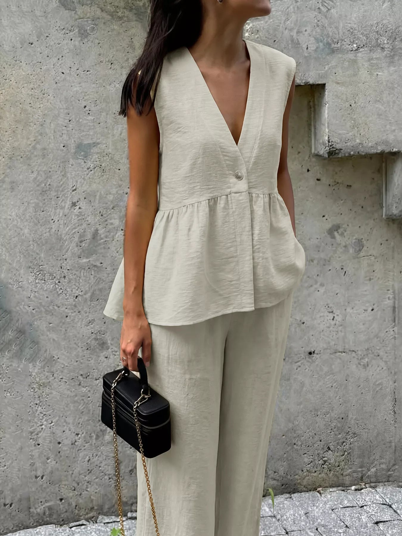 Woman wearing a beige sleeveless top and pants against a concrete wall.