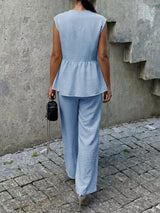 Person wearing a light blue sleeveless top and pants against a gray wall.