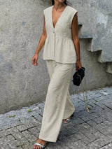 Woman wearing a beige sleeveless top and pants against a concrete wall.