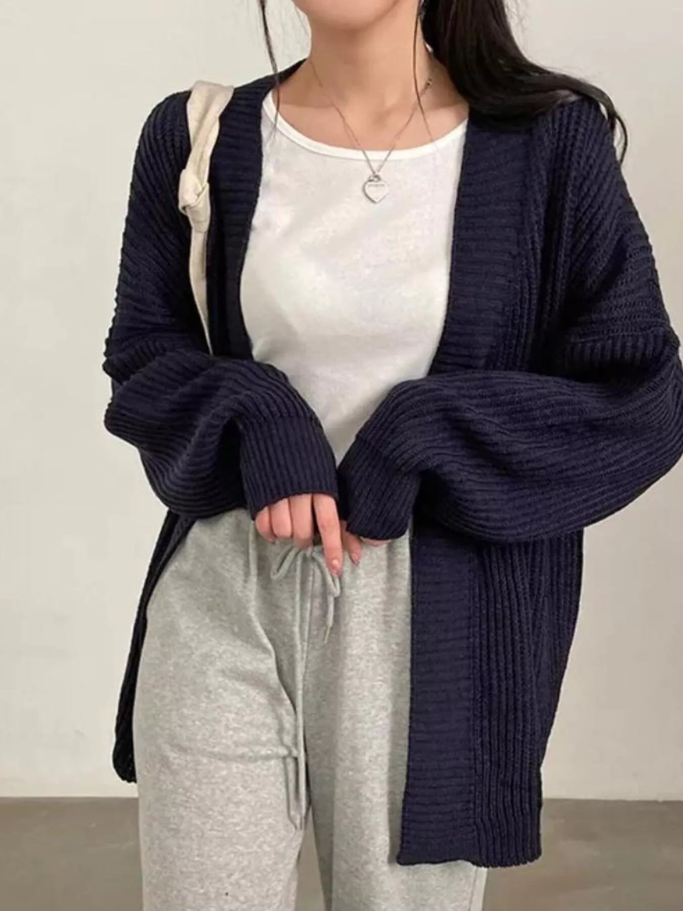 Women's black open front oversized ribbed knit cardigan layered over a white tank top with black pants, cozy fall sweater for casual everyday style.
