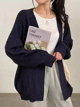 Women's black open front oversized ribbed knit cardigan layered over a white tank top with black pants, cozy fall sweater for casual everyday style.