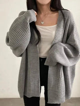 Women's gray open front oversized ribbed knit cardigan layered over a white tank top with black pants, cozy fall sweater for casual everyday style.