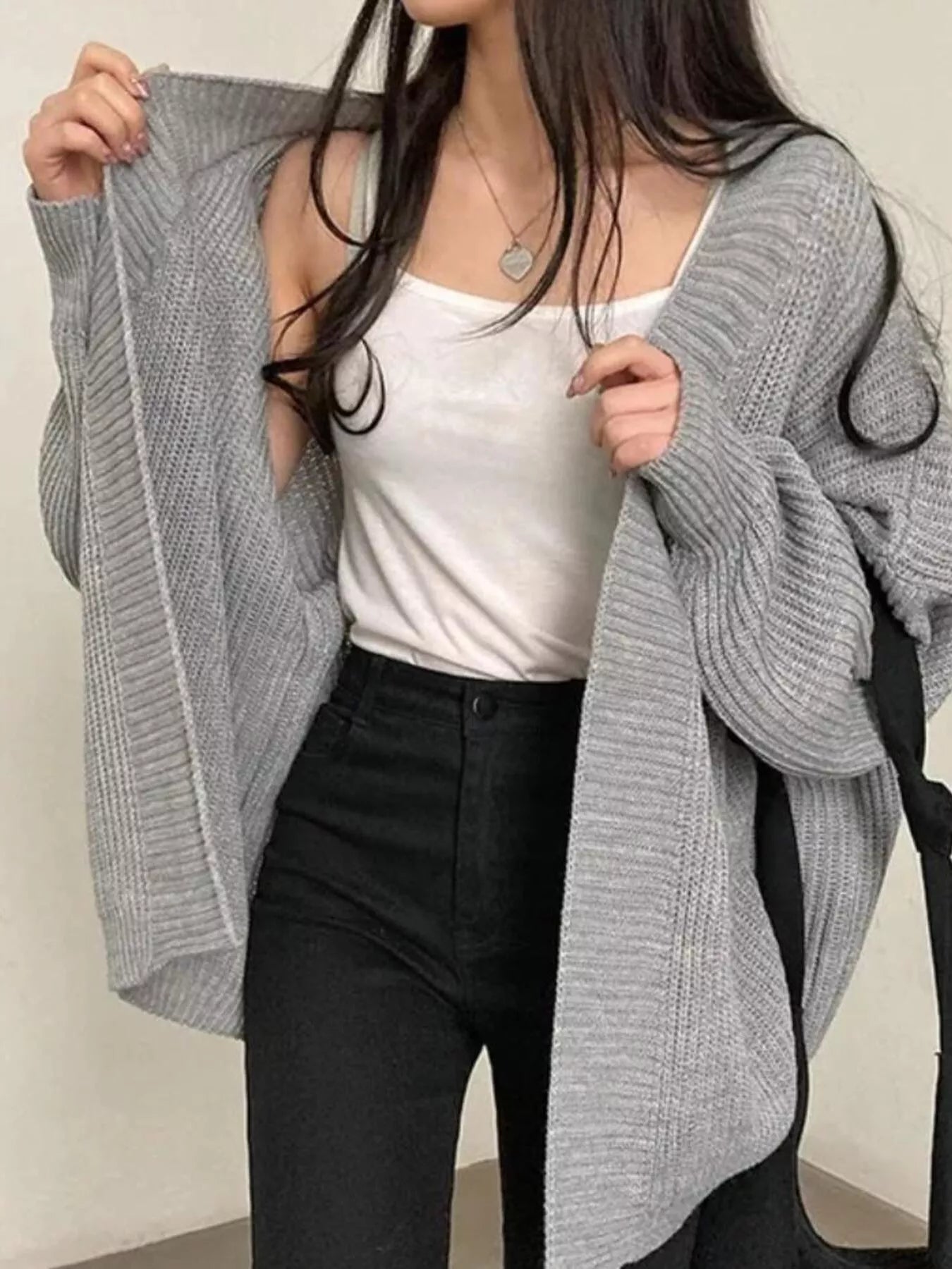 Women's gray open front oversized ribbed knit cardigan layered over a white tank top with black pants, cozy fall sweater for casual everyday style.