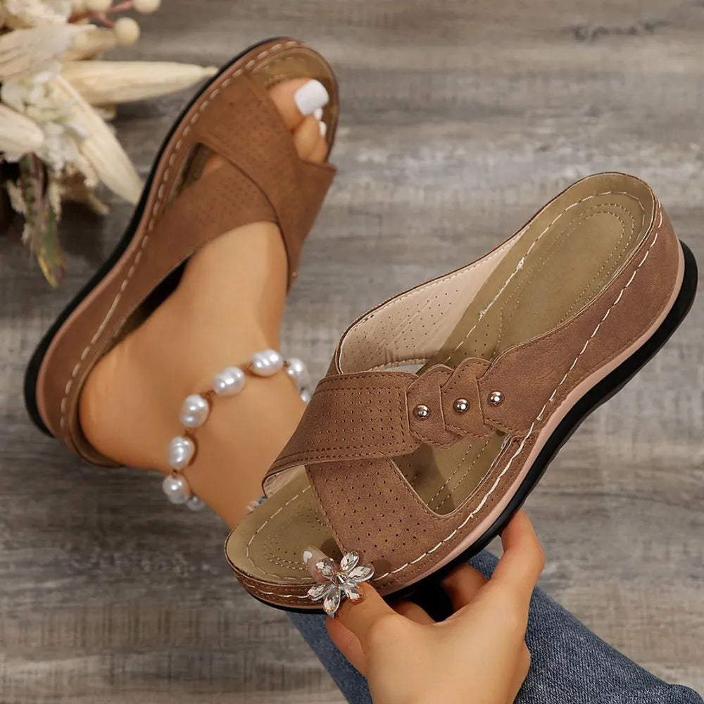 Brown sandals with decorative elements held by a hand on a wooden surface