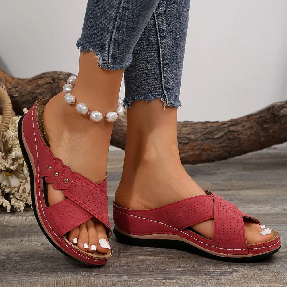 Red sandals worn with denim jeans on a wooden surface.