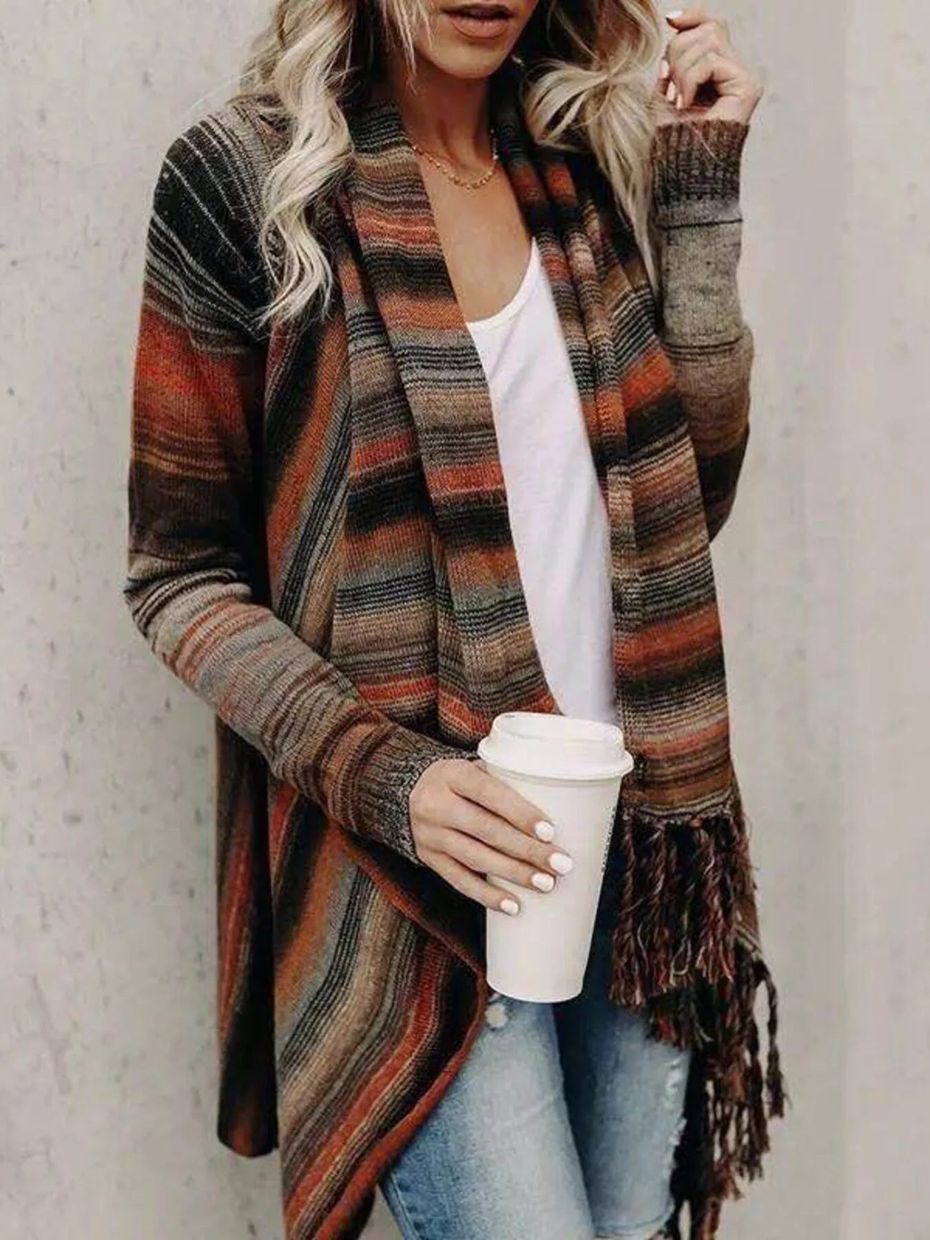 Woman wearing an orange stripe fringe long sleeve wrap cardigan with an asymmetrical draped front over a white top and jeans.