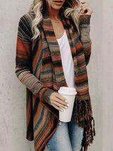 Woman wearing an orange stripe fringe long sleeve wrap cardigan with an asymmetrical draped front over a white top and jeans.