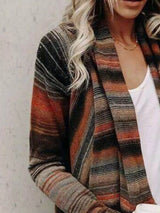 Woman wearing an orange stripe fringe long sleeve wrap cardigan with an asymmetrical draped front over a white top and jeans.
