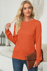 Woman wearing an orange textured round neck long sleeve blouse with dark-wash jeans and brown clutch.