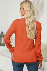 Woman wearing an orange textured round neck long sleeve blouse with dark-wash jeans.
