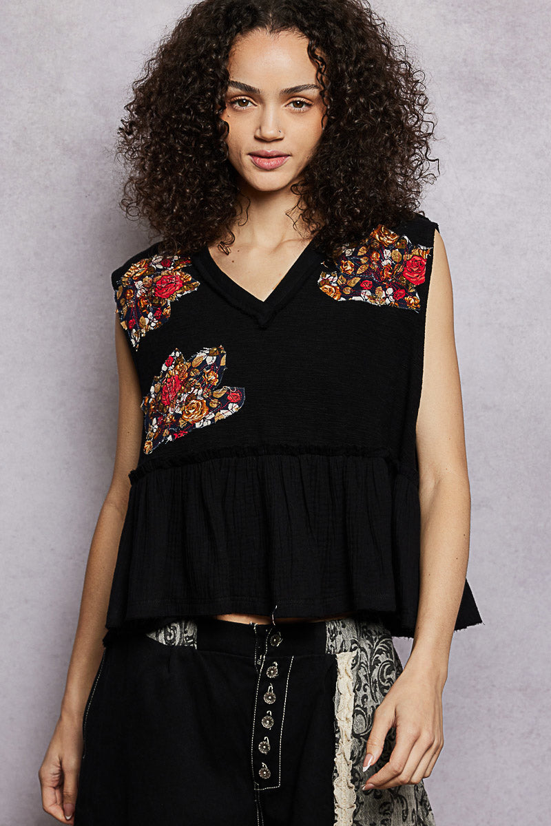 Woman wearing a black sleeveless top with floral embroidery against a gray background