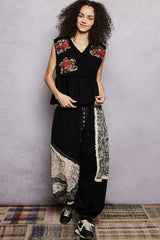 Woman wearing a black outfit with floral embroidery against a gray wall.