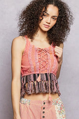 Woman wearing a pink lace-up top with fringe details against a gray background