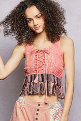 Woman wearing a pink lace-up top with fringe details against a gray background