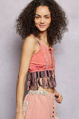 Woman wearing a pink top with fringe and a matching skirt against a gray background