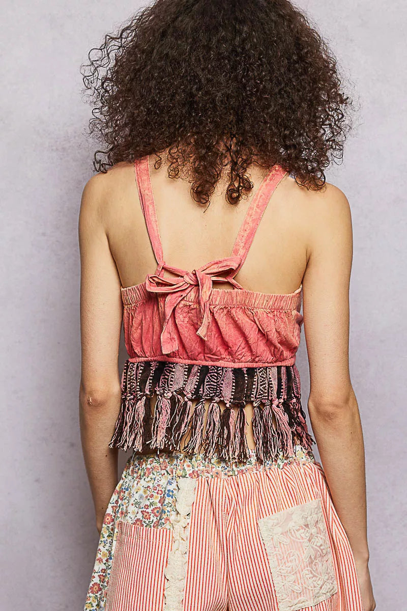 Person wearing a pink top with fringes and floral pants against a gray background