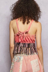 Person wearing a pink top with fringes and floral pants against a gray background