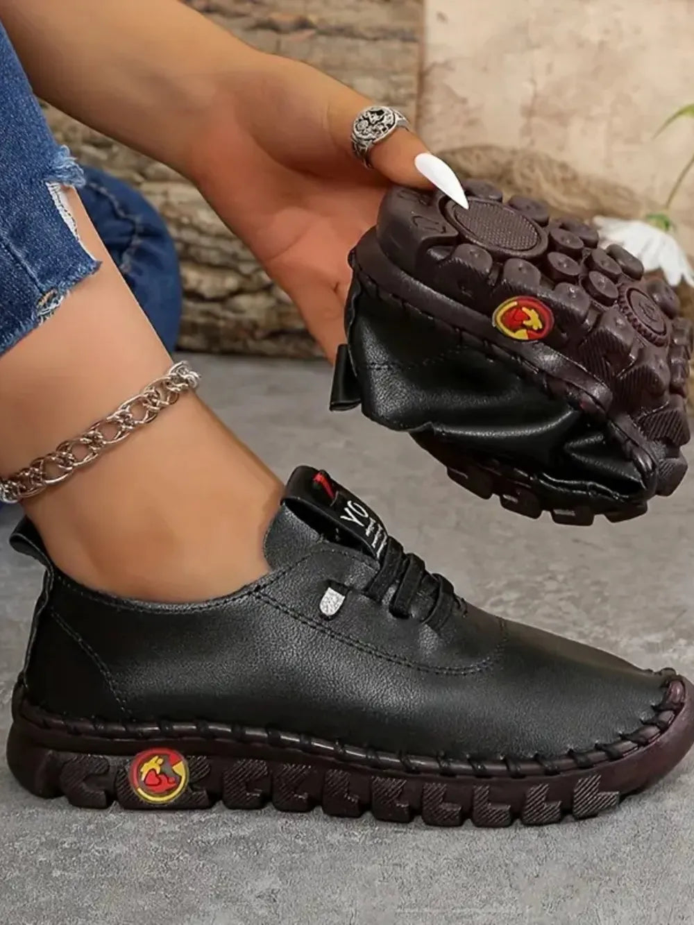 Black leather shoes with red and yellow logos being held by a person wearing blue jeans.