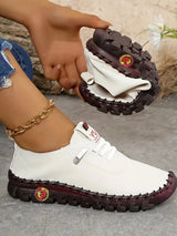 White shoe with brown sole held by a hand, with a small bag in the background.