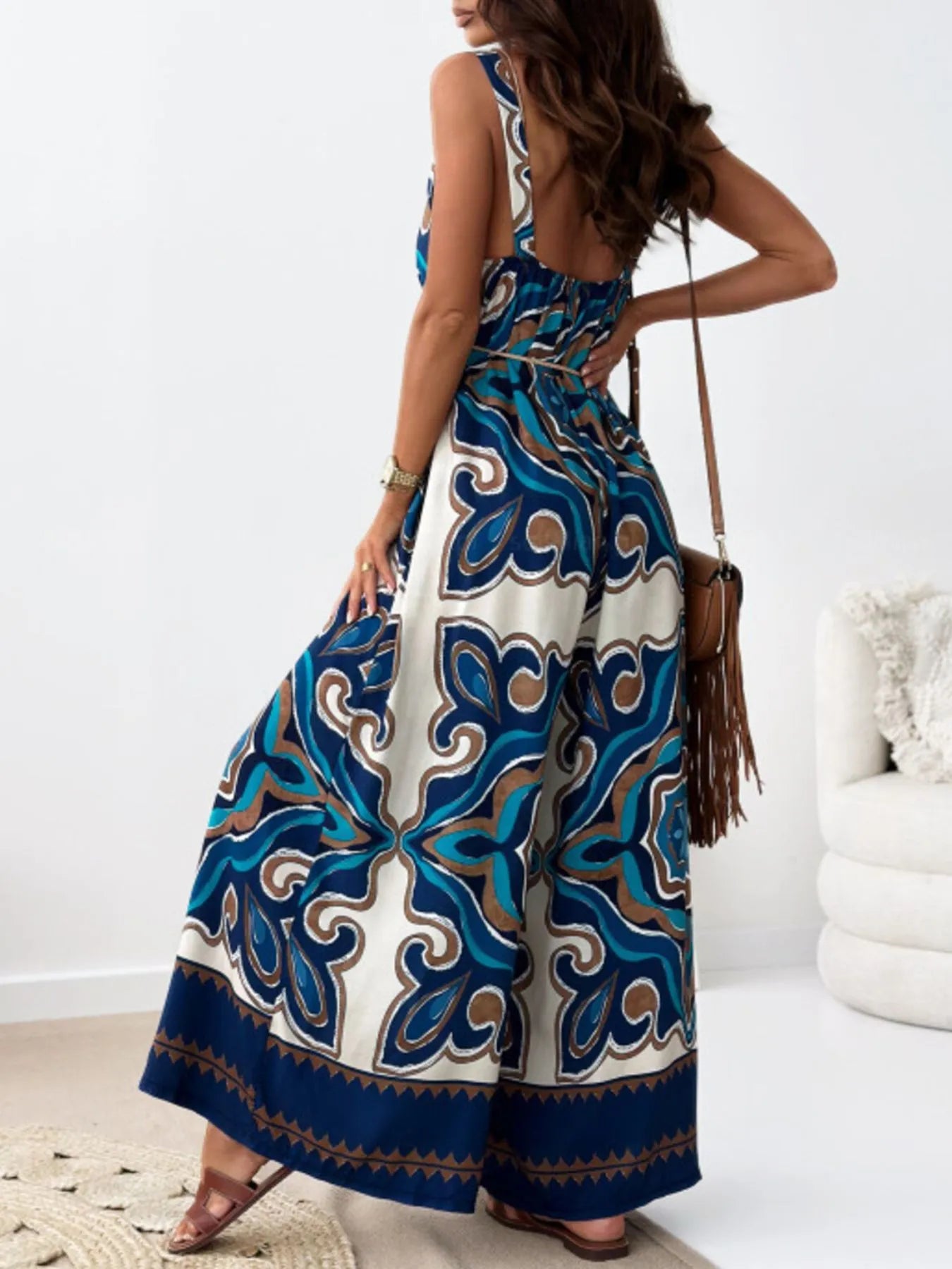 Woman wearing a sleeveless jumpsuit with a blue and white pattern in a minimal indoor setting.