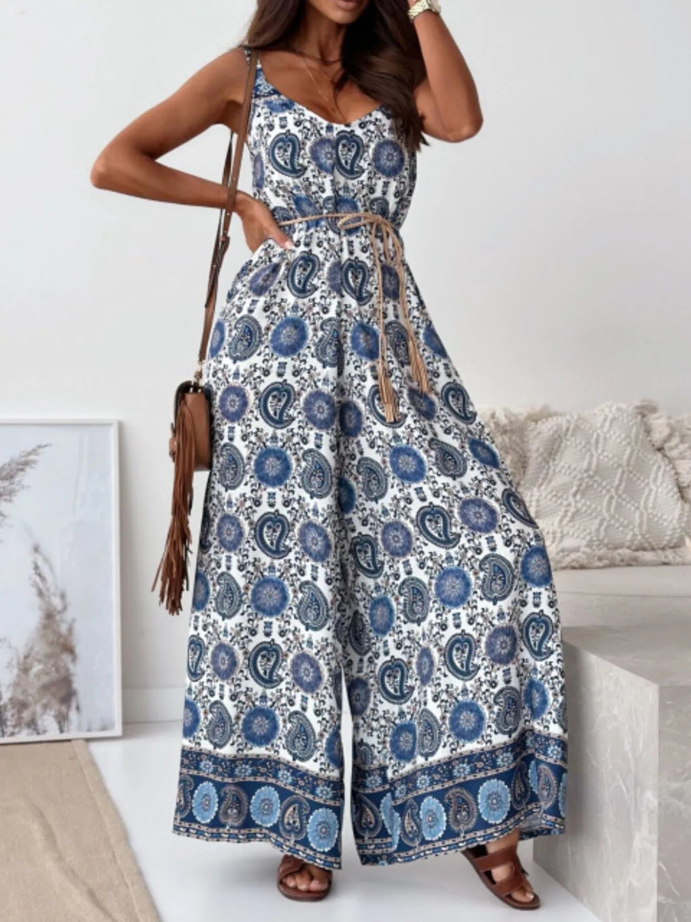 Woman wearing a blue and white feathered patterned jumpsuit in a minimal indoor setting.