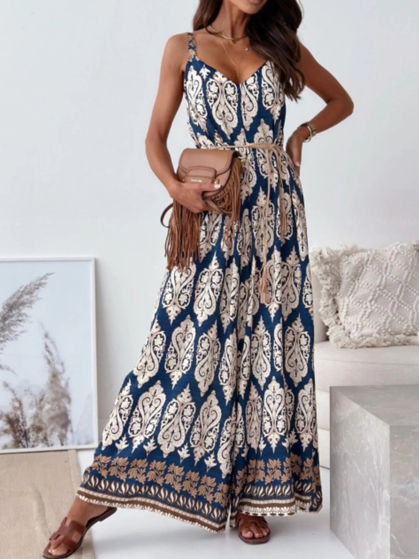 Woman wearing a blue and white patterned jumpsuit holding a brown handbag indoors.