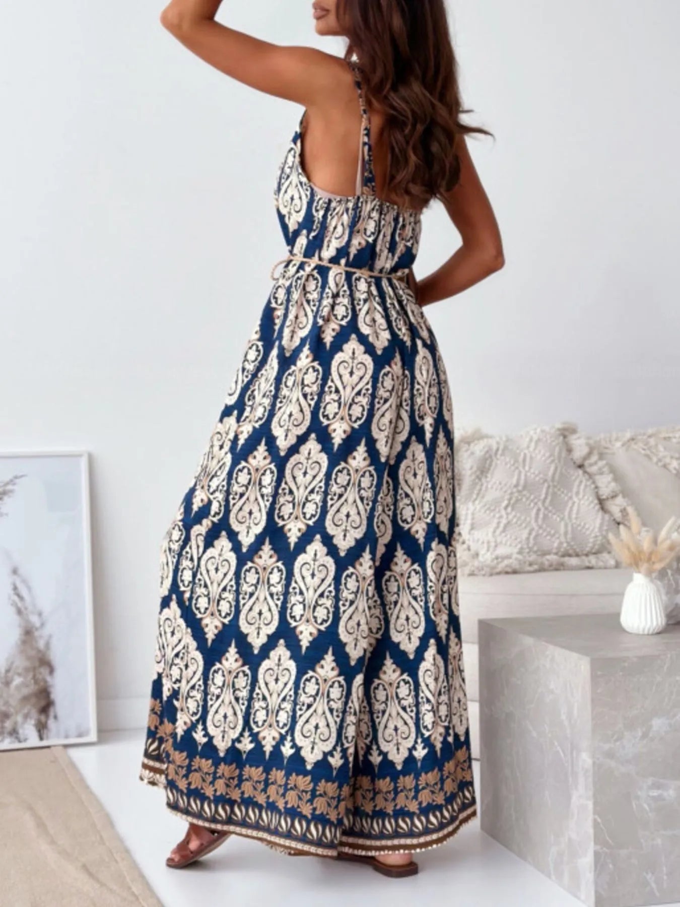 Woman wearing a blue and white patterned jumpsuit in a minimalistic room showcasing the back.