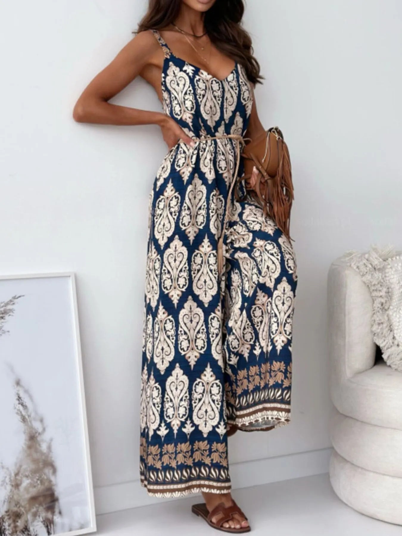 Woman wearing a blue and white patterned jumpsuit in a room with a white wall and chair.