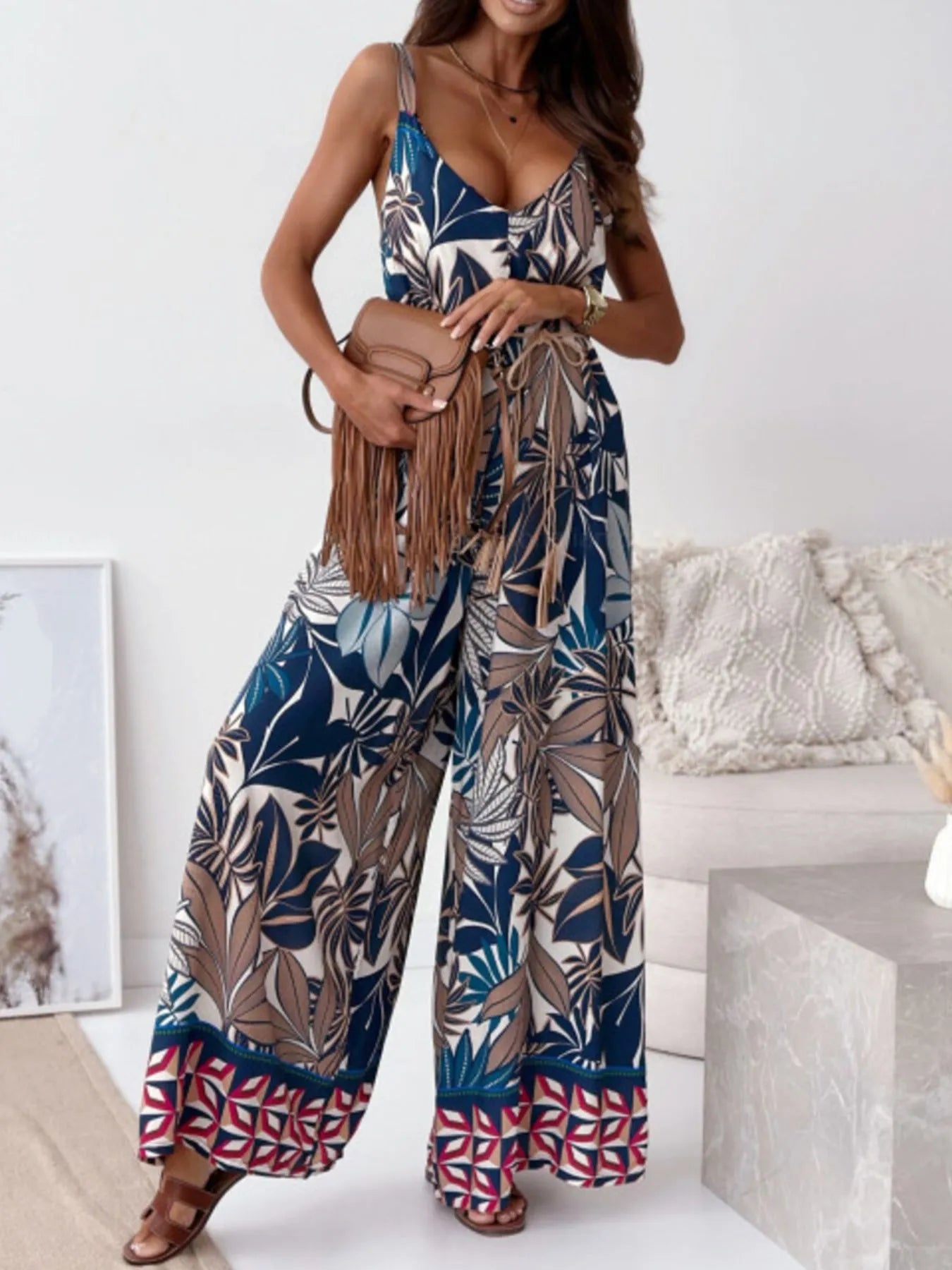 Woman wearing a big leaves patterned jumpsuit holding a brown handbag in a minimalistic room.