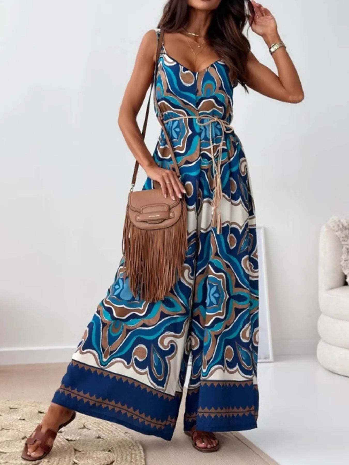 Woman wearing a blue patterned jumpsuit holding a brown handbag indoors.