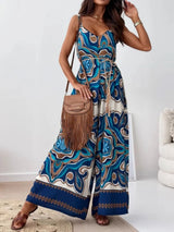 Woman wearing a blue patterned jumpsuit holding a brown handbag indoors.