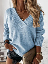 Woman wearing a pastel blue V-neck long sleeve knit top with ribbed neckline and cuffs, styled with black denim shorts.