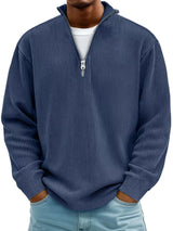 Man wearing a peacock blue ribbed corduroy quarter zip pullover sweatshirt layered over a white shirt.