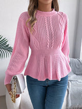 Woman wearing a pink cable knit round neck peplum sweater with long sleeves and blue jeans.