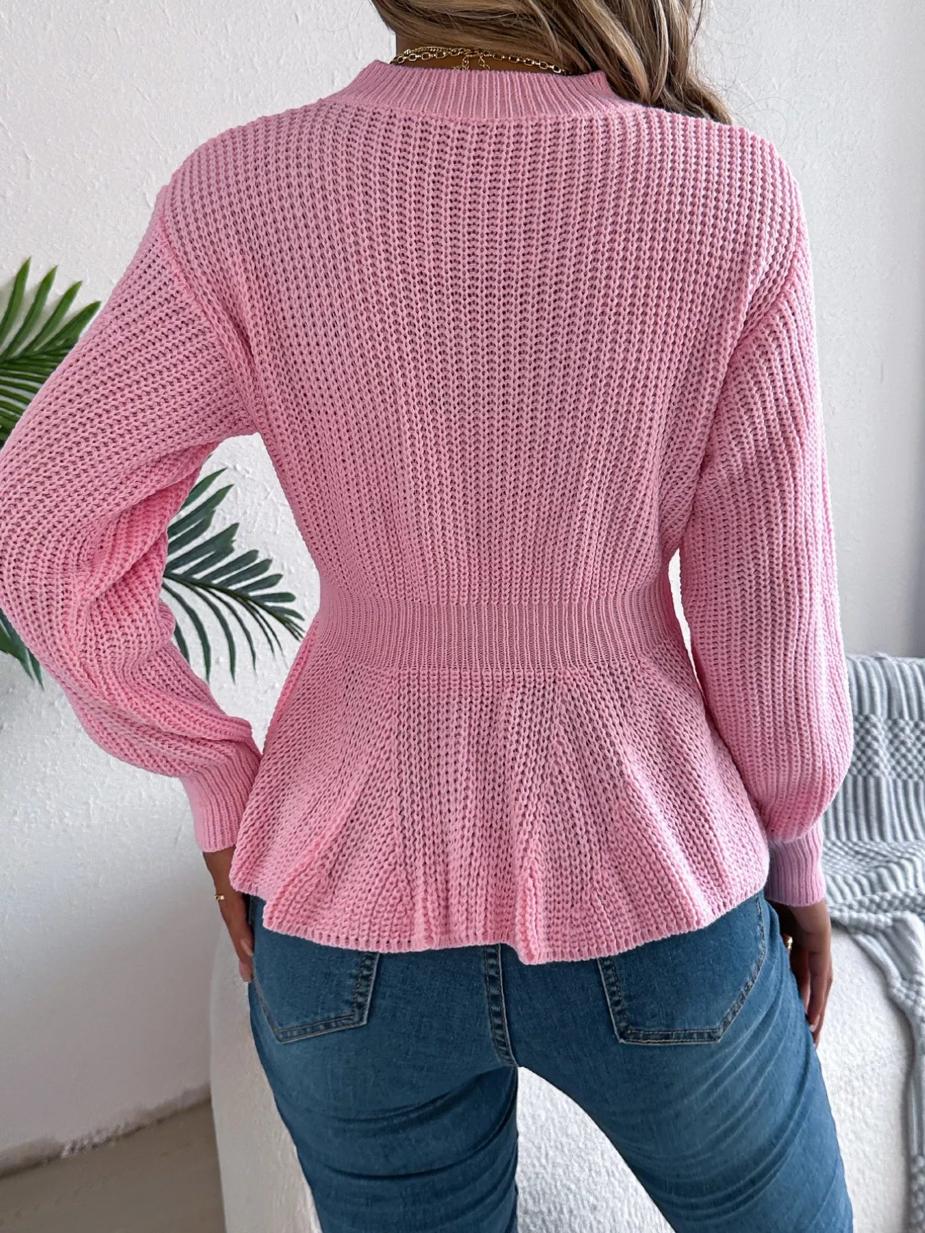 Woman wearing a pink cable knit round neck peplum sweater with long sleeves and blue jeans.