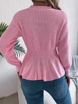 Woman wearing a pink cable knit round neck peplum sweater with long sleeves and blue jeans.