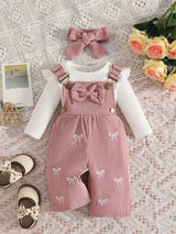Baby girl three-piece outfit featuring a cream ribbed long-sleeve bodysuit with ruffled shoulders, pink bow-embroidered overalls and matching pink bow headband.