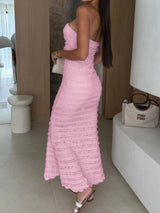 Woman wearing a pink sweetheart neck tube maxi dress with ruched detailing and a subtle cutout, styled with an ivory clutch for an elegant evening look.